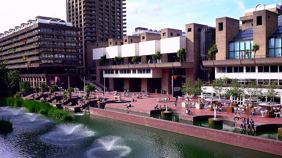 Barbican Centre in Autumn in London, a brutalist building built on the side of a river, with people milling around in the background.